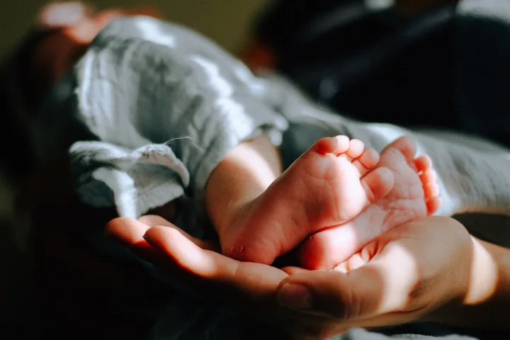 Pies de un bebé sostenidos con cuidado por sus padres